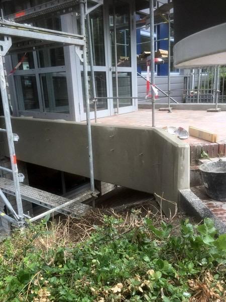 Betonpodest am Gebäudeeingang während der Instandsetzung, eingerüstet
