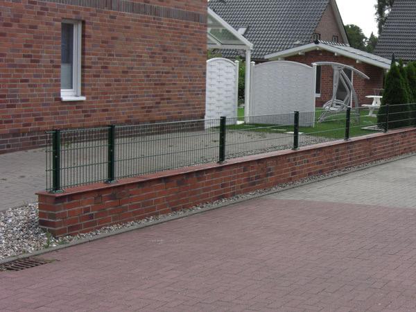 Niedrige Klinkermauer mit Stabzaun entlang der Hofeinfahrt