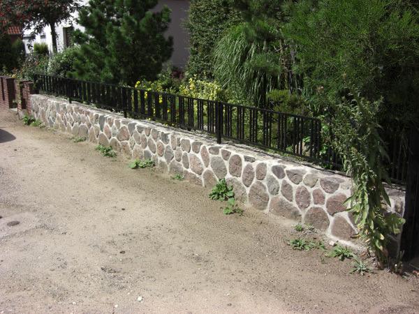 Feldsteinmauer als niedrige Stützmauer mit Metallzaun