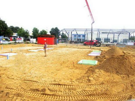 Baugrube mit vorbereiteten Fundamenten, im Hintergrund die Betonpumpe