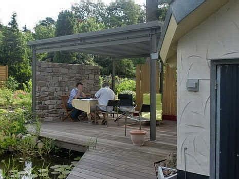 Überdachte Terrasse mit Natursteinmauer und Teich am umgebauten Haus